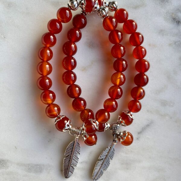 carnelian beaded bracelet with silver feather charm on a marble surface