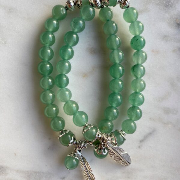 green aventurine beaded bracelet with silver feather charm on a marble surface
