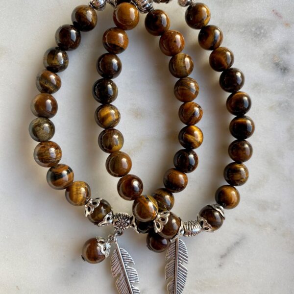 tigers eye beaded bracelet with silver feather charm on a marble surface