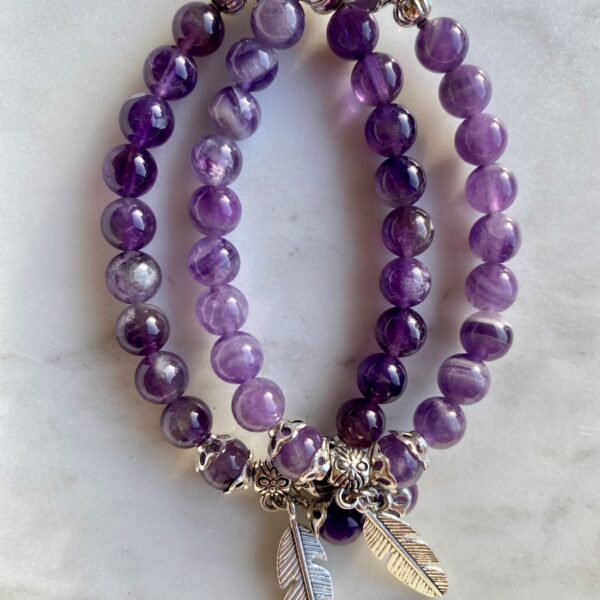 amethyst beaded bracelet with silver feather charm on a marble surface
