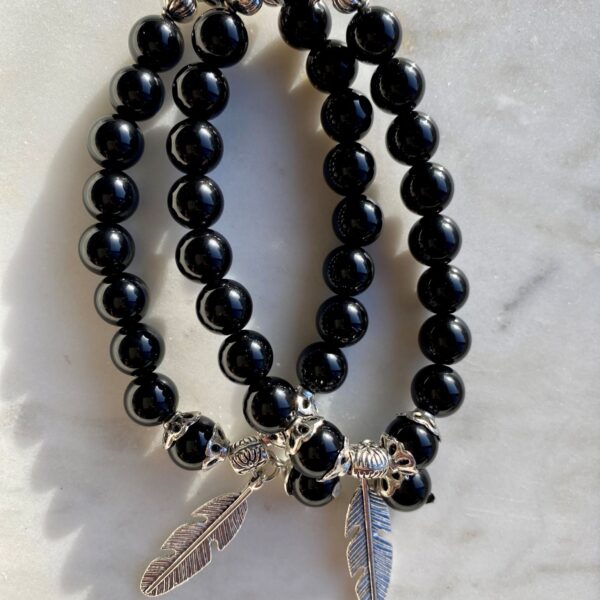 black obsidian beaded bracelet with silver feather charm on a marble surface