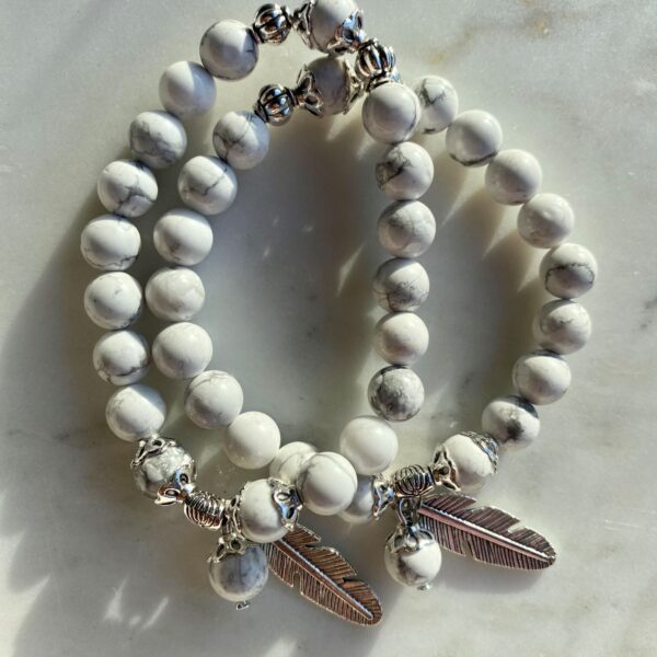 howlite beaded bracelet with silver feather charm on a marble surface